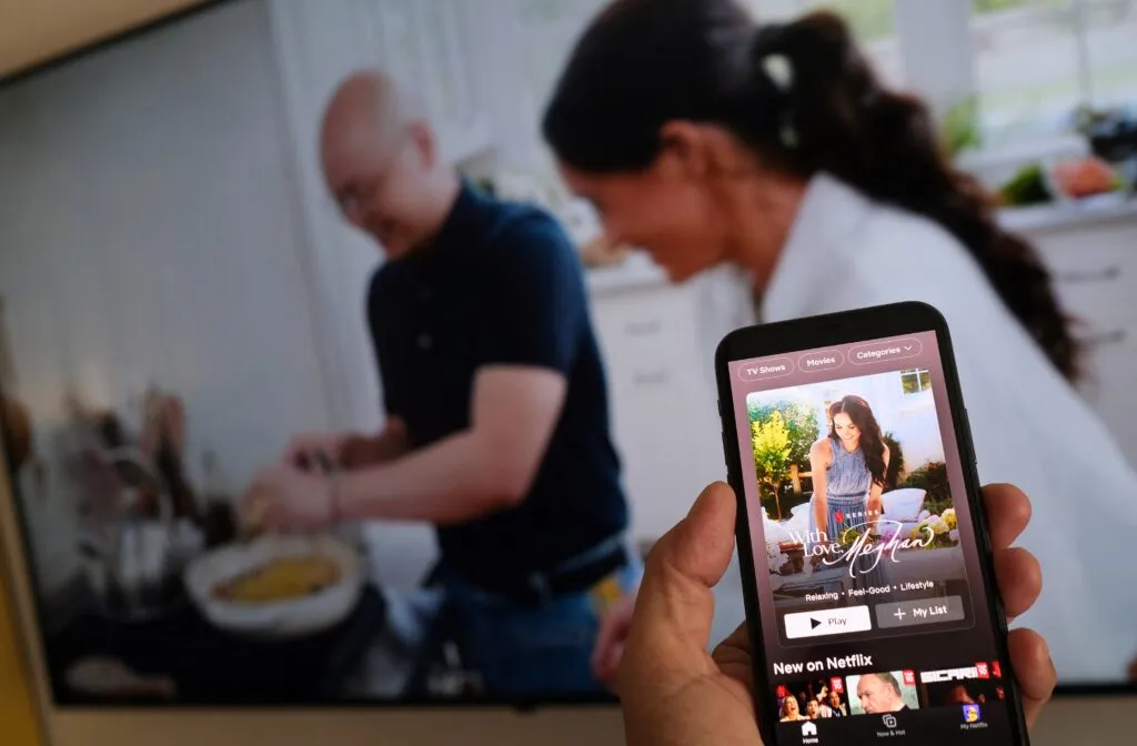 A person holds a smartphone displaying Netflix’s Meghan Markle show, “With Love, Meghan”, in front of a TV screen in Los Angeles